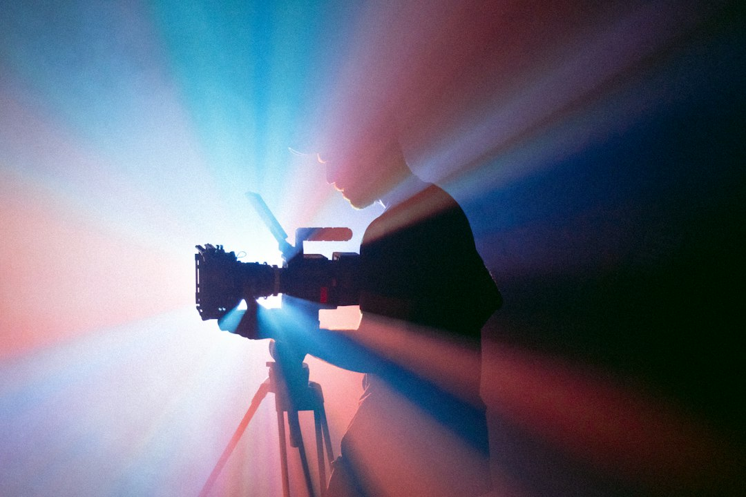 Camera operator filming with a camera on a tripod under colored lights
