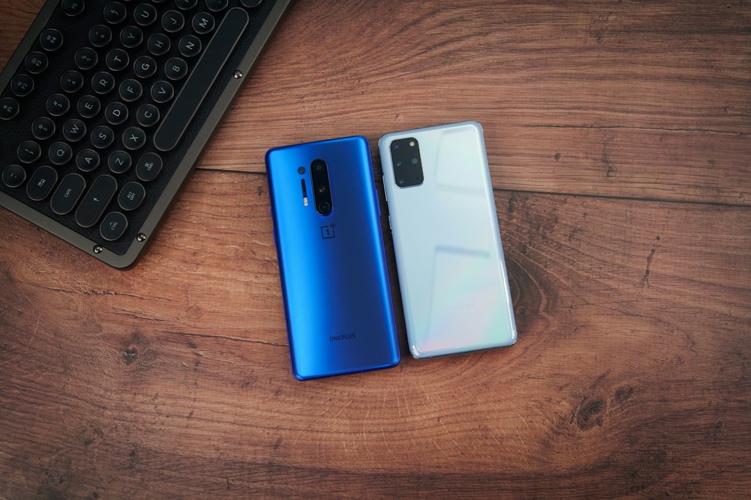 Two smartphones beside a keyboard on a wooden desk