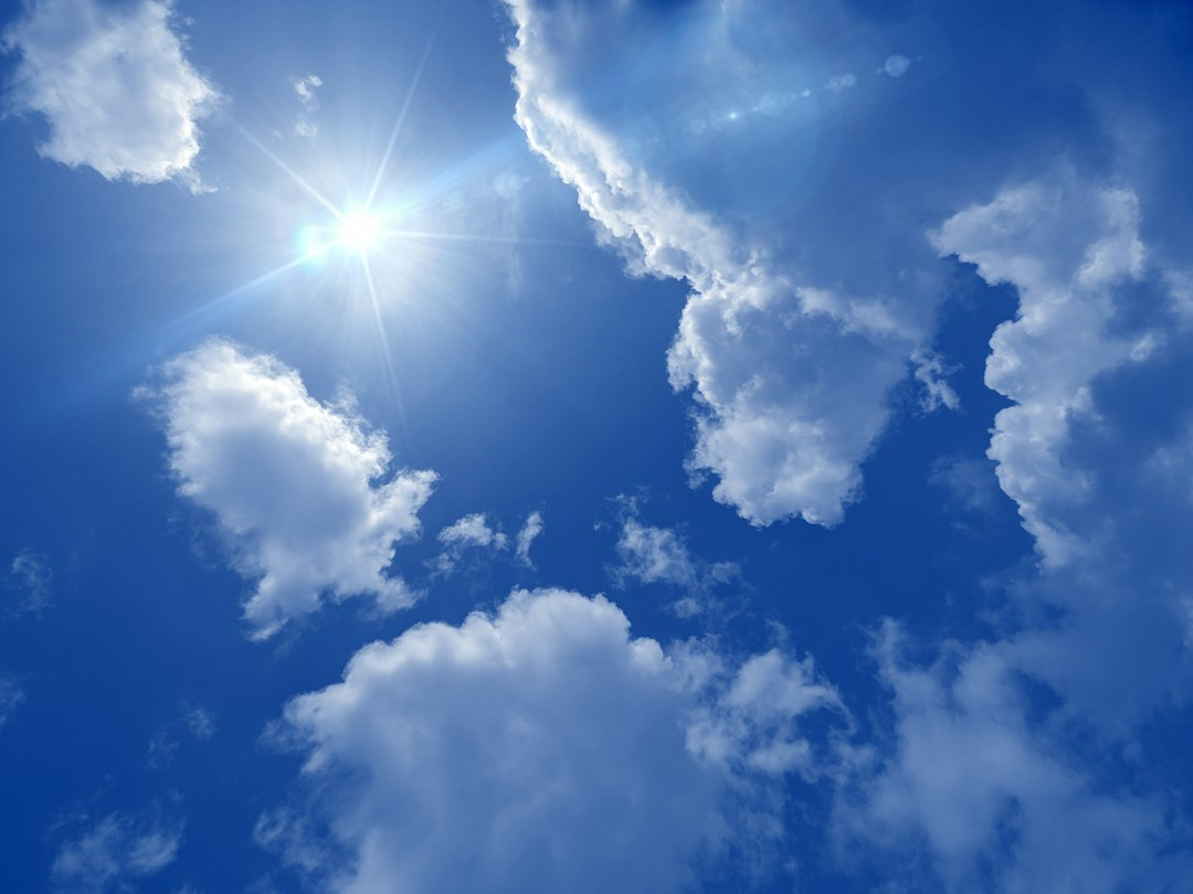 Sunlight shining through white clouds in a bright blue sky