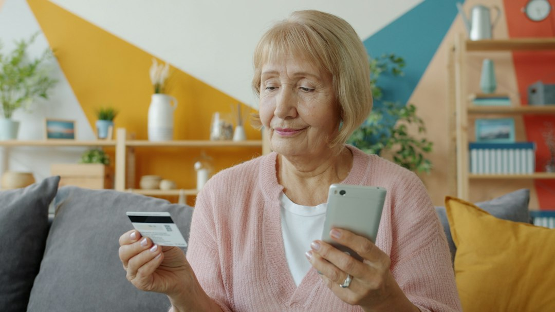 Older woman using a bank card and smartphone at home